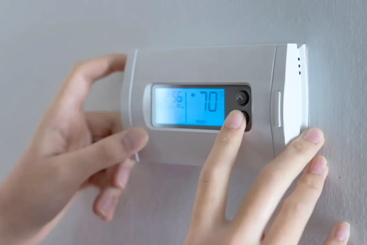 Hands adjusting a digital wall thermostat